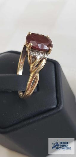 Gold colored ring with a large dark red gemstone, clear gemstones on side, twisted band, marked 14K,