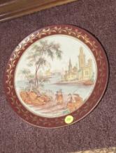 (DEN) 10"D DECORATIVE PLATE, DEPICTS A RIVER, BUILDINGS AND PEOPLE.